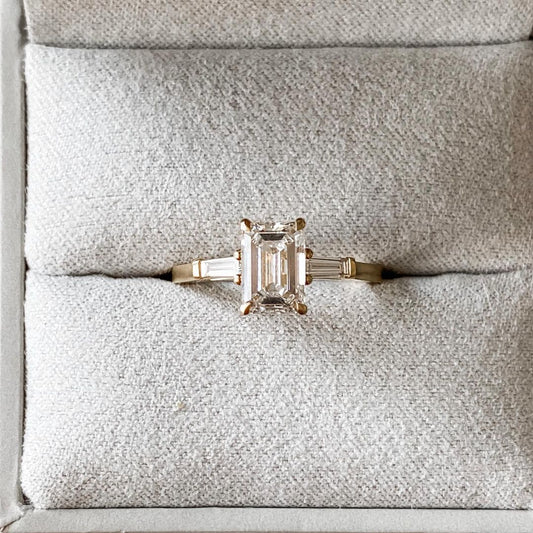 2.5ct Emerald Center Stone With Two Side Baguette Stone Lab Grown Diamond Ring youtube google instagram Elegant close-up of a hand showcasing an engagement ring with a gold band, ideal for proposals, weddings, or luxury jewelry collections, paired with a soft, natural manicure.